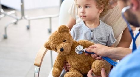 Arzt hört den Teddy eines Kleinkinds wird ab.